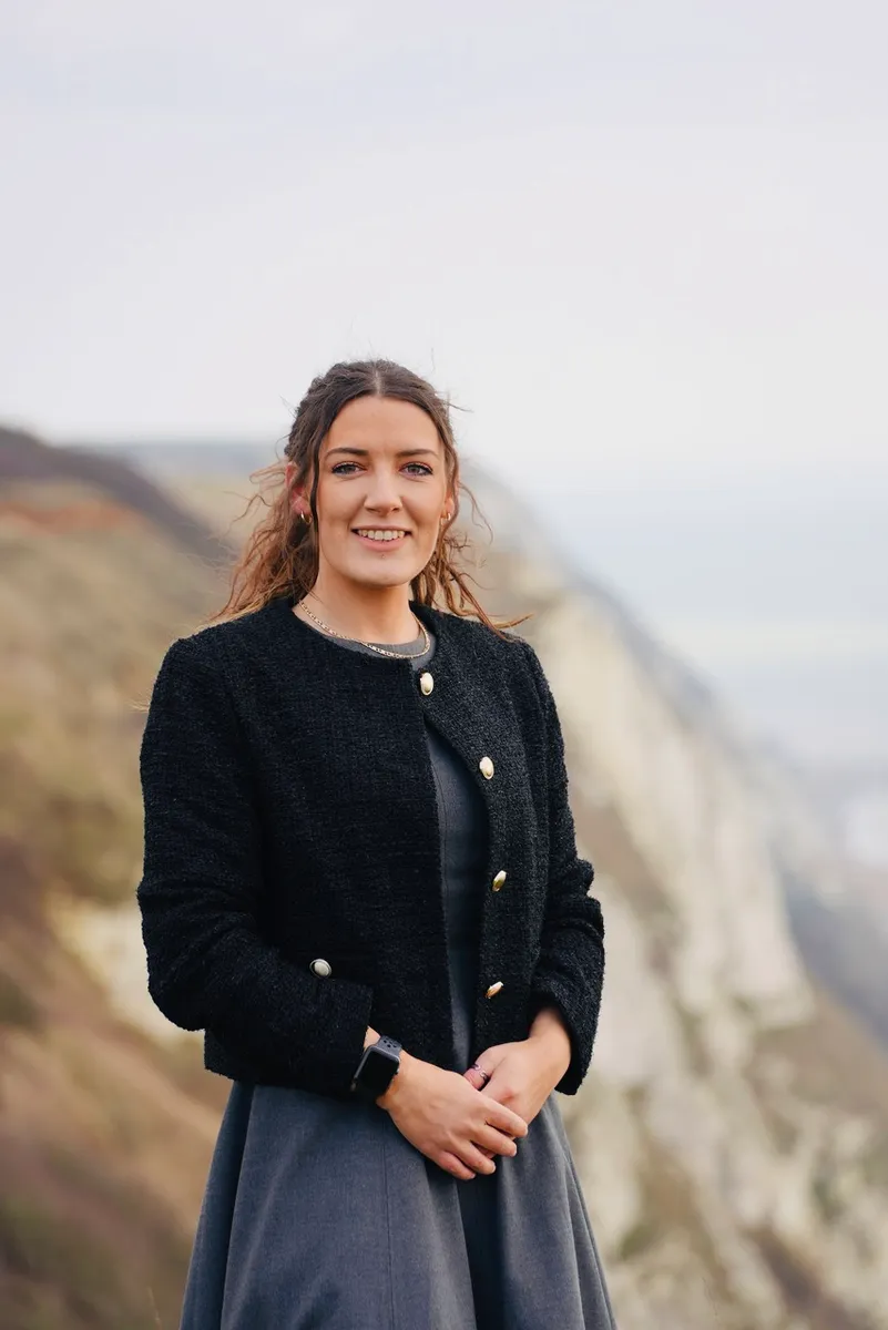 Cassandra Sinclair smiling on a clifftop, with the sea behind her